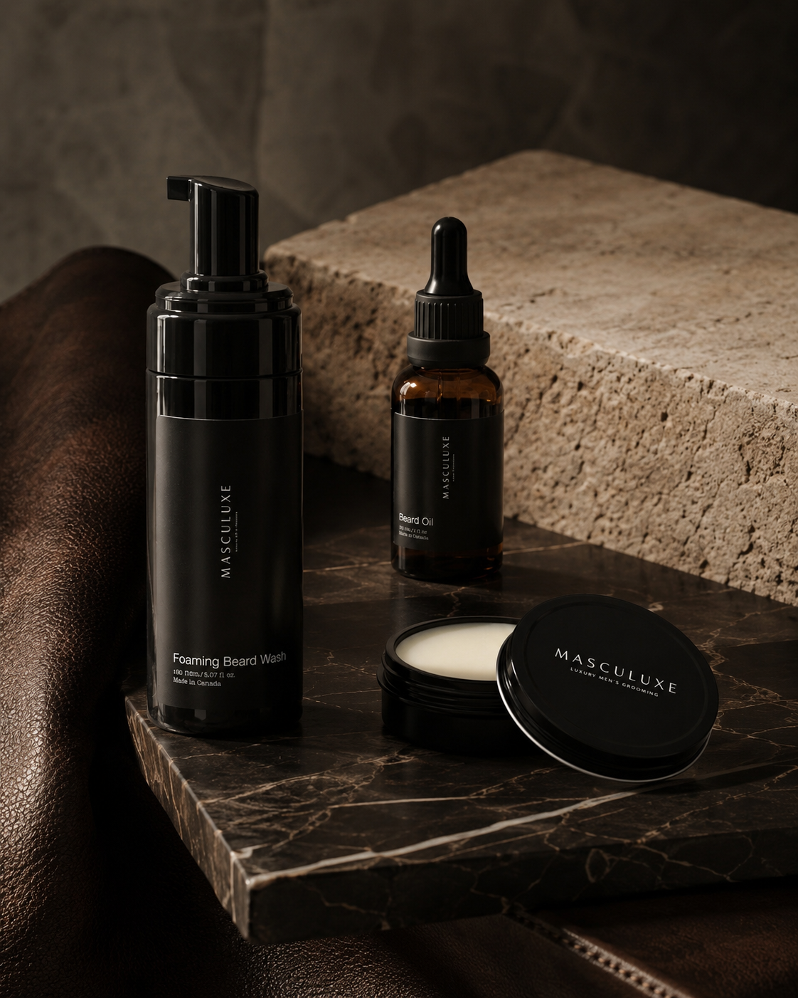 A set of four beard care products from the brand MASCULUXE, including a Foaming Beard Wash, a Beard Oil, and a Beard Balm, arranged on a dark marble tray with a leather surface and a stone block background.