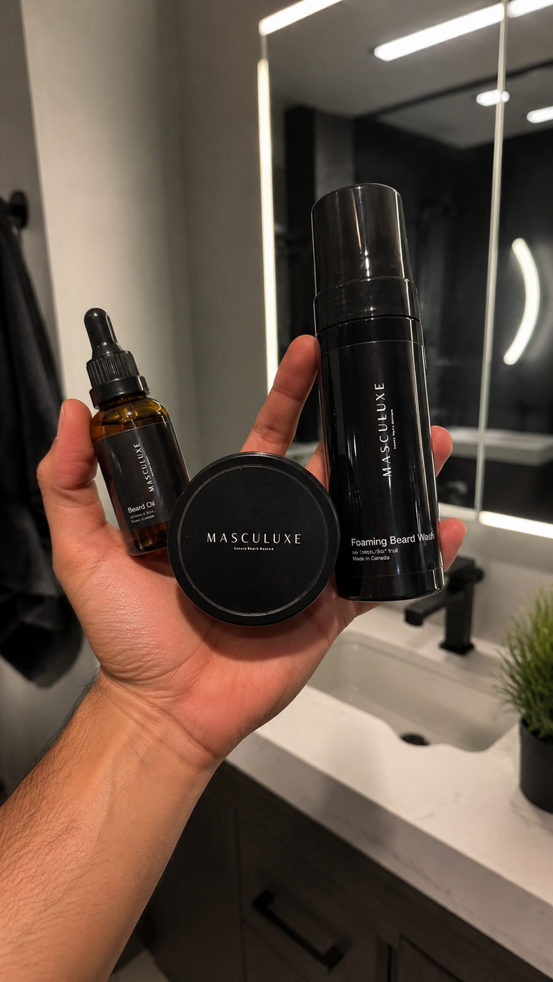 Hand holding three Masculuxe grooming products in a bathroom setting